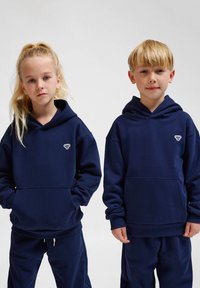 Marinblå hoodie i mjukt tyg med framfickor och ribbad mudd, med en liten vit logotyp på vänster bröst.