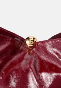 Rode glanzende leren clutch met een gouden ronde sluiting in het midden bovenaan. Kenmerkt zich door een gekreukt textuur en een gladde afwerking.