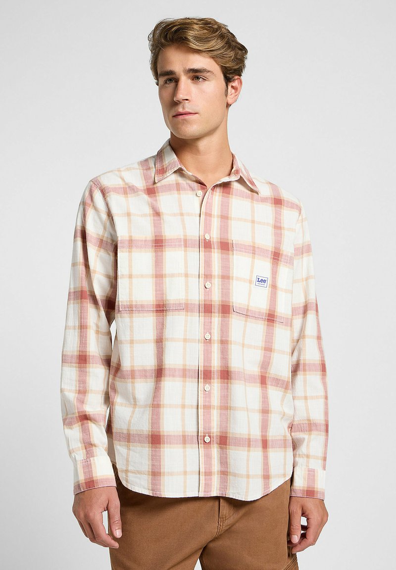 Camisa de cuadros de manga larga en colores crema, rojo y durazno; cuenta con un cuello abotonado, bolsillo en el pecho y una textura de tela suave.