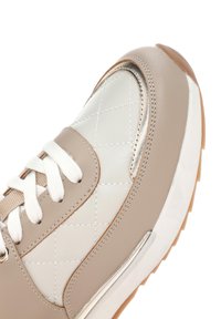 Beige sneaker with quilted light gray leather panels, white laces, and metallic accents. Features a rubber sole with textured grip.