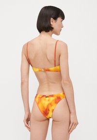 Bikini-set i en livlig gul og oransje tie-dye mønster, med slanke justerbare stropper og en lås i ryggen. Ribbet tekstur.