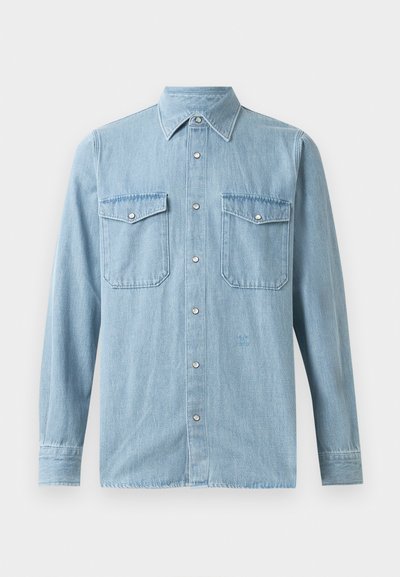 Lyseblå denimskjorte med knappelukking foran, spiss krage, to brystlommer og knappefeste vedermansjettene. Jevn tekstur med minimal detaljering.