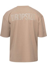 T-shirt beige, coupe oversize, col rond, manches courtes, avec le mot "DROPSIZE" imprimé en gras, texte gris clair au dos.