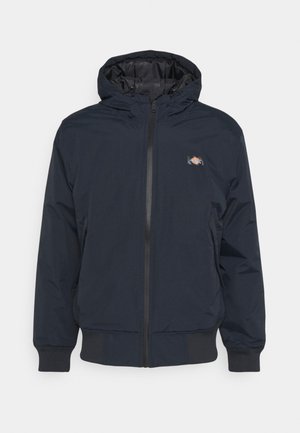 Mørkeblå lynlåsjakke med hætte, elastiske manchetter, taljeafslutning og lille logopatch på venstre bryst.