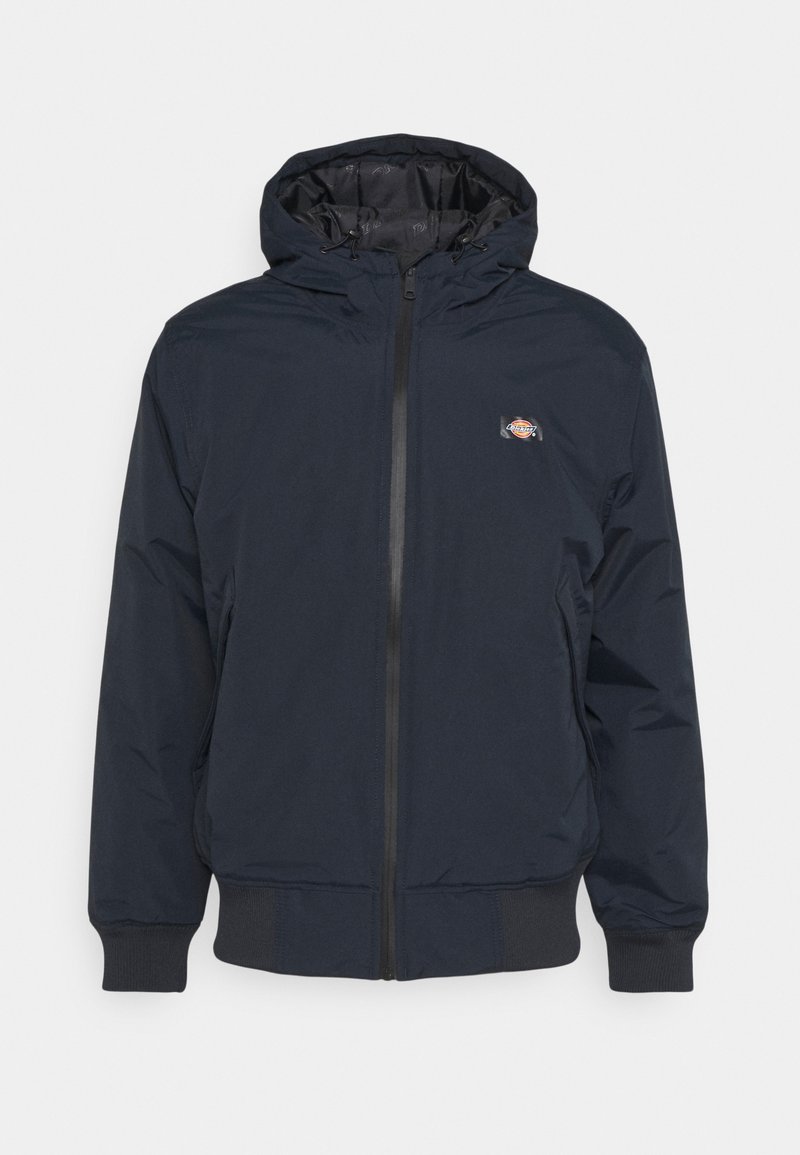 Veste zippée bleu marine avec capuche attachée, poignets élastiques, ourlet à la taille et petite écusson logo sur la poitrine gauche.