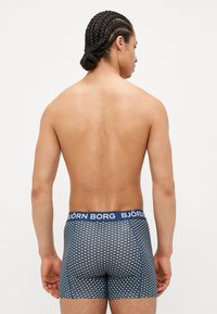 Marineblaue Boxershorts mit geometrischem Muster und einem elastischen Bund mit Markenlogo. Der Stoff wirkt weich und dehnbar.