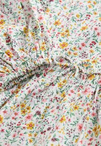Blumenmuster-Detail in leichtem Stoff. Verfügt über eine Raffung an der Taille mit kleinen rosa, gelben und grünen Blumenmustern auf einem weißen Hintergrund.