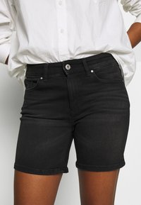 Pantalones cortos de mezclilla negra con un diseño ajustado, que cuentan con cierre de botones, bolsillos delanteros y un dobladillo que termina a mitad de muslo.