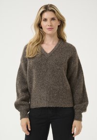 Pulover tricotat texturat, de culoare maro, cu decolteu în V, croială largă și tiv împletit. Mâneci lungi, ușor puffate și un aspect moale și confortabil.