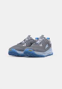 Graue Trailrunning-Schuhe mit Obermaterial aus Mesh und Synthetik, blauen Akzenten und Vibram-Außensohle. Merkmale sind flache Schnürsenkel und eine gepolsterte Sohle.