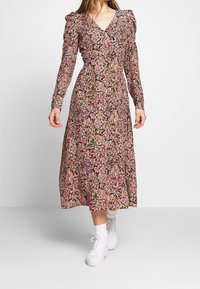 Blommig midiklänning med långa puffärmar, djup V-ringning och samlad midja. Flerfärgad tryck på mörk bakgrund, i kombination med vita sneakers.