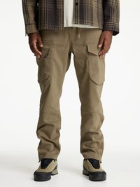 Bruna cargobyxor med sidofickor, tillverkade av slitstarkt material. Kombineras med svarta och beige skor med strukturerade ytor och snörning.