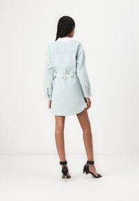 Lyseblå denimkjole med lange ermer, belte i midjen, og buet kant, med hvit krage og tonede sømmer.