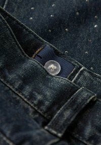 Denimjeans i en djupblå färg, med en genomskinlig plastknapp och en texturerad yta med silverprickmönster.
