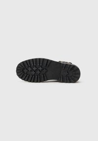 Suela de bota de goma negra con surcos profundos que presentan patrones en cruz y rectangulares; superficie texturizada para una mejor adherencia y durabilidad.