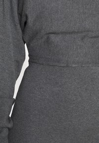 Grau gestrickter Stoff mit geripptem Muster und taillierter Form. Das Bild zeigt den Übergang von einem glatten Abschnitt zu einem gerippten Bund.