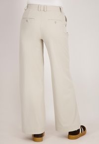 Lichtbeige wijde broek van een zachte stof, met twee achterzakken met knopen en lussen voor een riem in de taille.