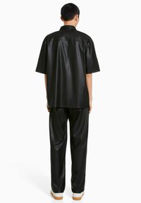Svart konstläder kortärmad skjorta och matchande byxor, med en avslappnad passform och en slät yta. Enkelt design utan synliga mönster.