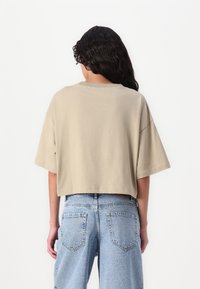 Beige cropshirt med korte ærmer, lavet af blødt stof. Kombinationen med lys blå højtaljede denimjeans med baglommer.