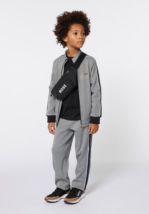 Survêtement à motif pied-de-poule en noir et blanc, avec une veste zippée et un pantalon rayé. Comprend un sac bandoulière noir avec le logo "BOSS".