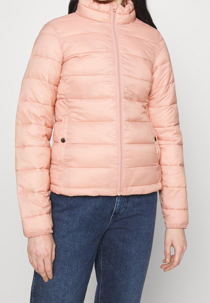 Giacca a vento rosa chiaro con colletto alto, cuciture orizzontali, zip frontale e due tasche laterali. Tessuto liscio con una finitura leggermente lucida.