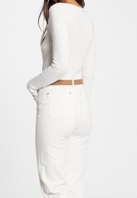 Bílý top s dlouhým rukávem z texturované látky, v kombinaci s bílými kalhotami s vysokým pasem a hnědým pásem. Na zádové části topu jemné detaily.