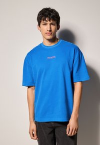 Blå bomulds T-shirt med afslappet pasform, korte ærmer og rund halsudskæring. Udsmykket med pink broderet tekst på brystet.