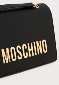 Must have musta nahast käekott, millel on silmatorkav kuldse tooni "MOSCHINO" logo, sujuva tekstuuri ja delikaatsete õmbluste detailidega.