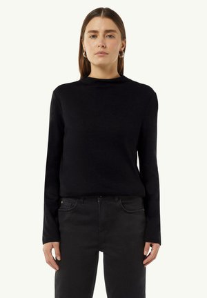 Zwarte lange mouw top met een hoge hals en een zachte textuur. Gecombineerd met donkere jeans, wat een monochrome look creëert.
