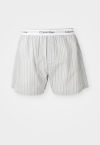 Baldos Calvin Klein vyriški bokseriai su plonomis vertikaliomis juodomis juostelėmis ir prekės ženklą turinčiu elastingu juosmeniu.