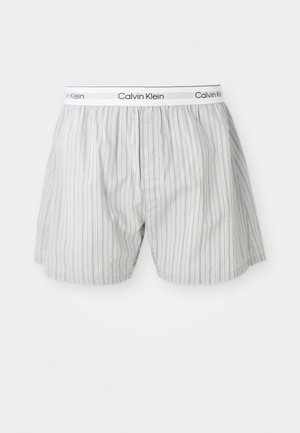 Baltas Calvin Klein vīriešu bokseršorti ar plānām vertikālām melnām svītrām un zīmola elastīgu vidukļa joslu.