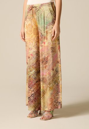 Pantaloni a gamba larga con motivi astratti e floreali multicolori, vita elastica con coulisse, abbinati a sandali con tacco alto e cinturini.