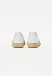 Scarpe bianche in pelle con suole in juta intrecciata, caratterizzate da un profilo basso e un tacco arrotondato. Texture liscia con cuciture sottili sui lati.