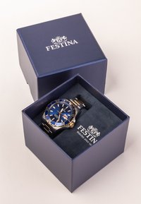 Montre FESTINA dans une boîte bleu foncé. La montre présente un cadran bleu, des accents dorés et un bracelet en acier inoxydable avec une surface texturée.