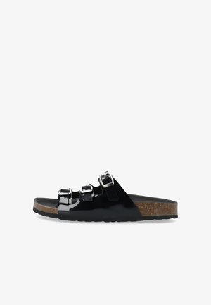 Sandal de charol negro tipo slide con tres hebillas ajustables, plantilla de corcho y suela plana de goma. Textura suave y diseño moderno.