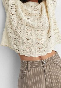 Haut court tricoté de couleur crème avec un motif en dentelle, associé à un pantalon taille haute rayé marron avec fermeture à boutons et poches.