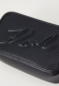 Pochette en cuir noir texturé avec le lettrage en relief "Karl" à l'avant, présentant une couture contrastante le long des bords.