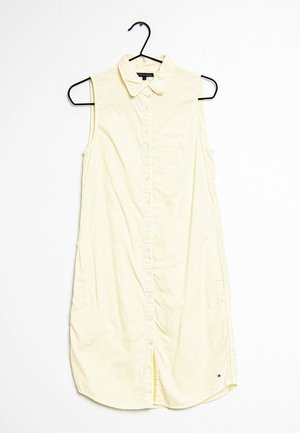 Geel mouwloos shirt met verticale witte strepen, knoopsluiting aan de voorkant, kraag en een borstzakje aan de linkerkant. Voorzien van zijopeningen aan de onderkant.