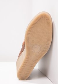Zapato de cuña con parte superior de cuero marrón texturizado, suela sintética beige y diseño de punta redonda. Destaca por su suave curvatura y un minimalismo en la marca.