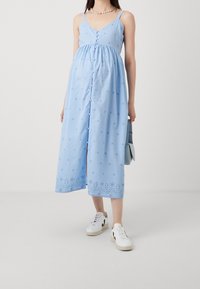 Ljusblå ärmlös klänning med en figursydd bodice, knapppdetalj och broderad stjärnmönster vid fållen. Matchad med vita sneakers.