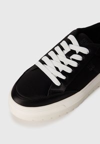 Sneaker in pelle nera con lacci bianchi e suola spessa bianca. Presenta una texture liscia, punta arrotondata e un sottile dettaglio del logo di lato.