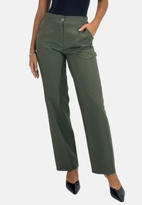 Khaki szerokie spodnie o gładkiej fakturze, z przednimi kieszeniami i pojedynczym zapięciem na guzik. W połączeniu z czarnymi, szpiczastymi szpilkami.