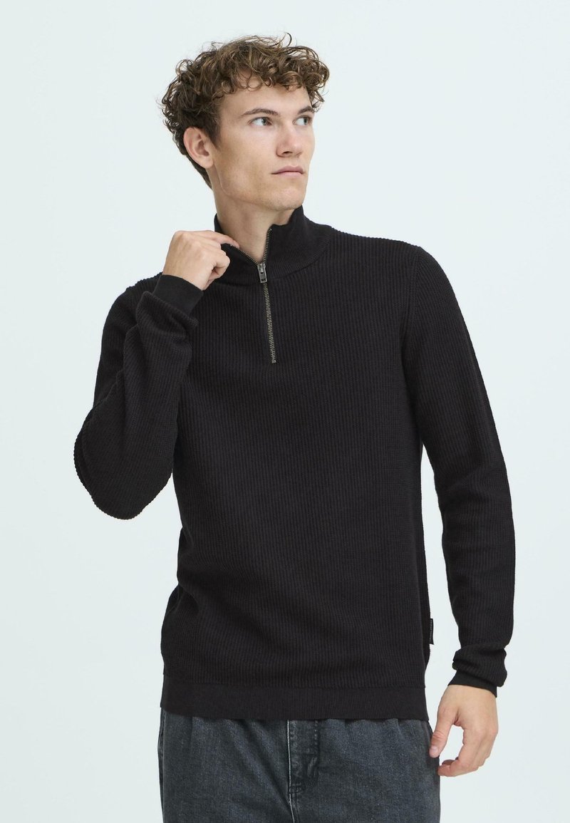 Pullover nero a coste con collo a zip a un quarto. Presenta maniche lunghe e orlo dritto. Realizzato in un tessuto morbido e testurizzato.