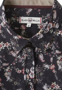 Blouse florale avec un fond noir, ornée de petites fleurs et feuilles multicolores, d'un col boutonné et de boutons noirs.