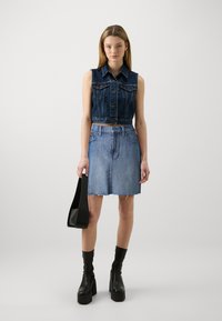 Chaleco de mezclilla cortado con un lavado oscuro, con botones y bolsillos, combinado con una falda de mezclilla en forma de A de color azul claro con dobladillo desflecado. Botas negras de plataforma.