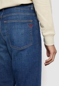 Dunkelblaue Denim-Jeans mit geradem Schnitt, sichtbaren Nähten und einem kleinen roten Logo auf der Gesäßtasche. Weiche Textur, standardmäßiges Fünf-Taschen-Design.