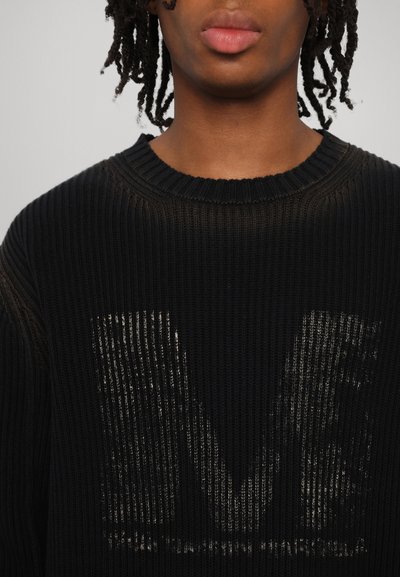 Svart ribbad tröja med rund halsringning, försedd med en urtvättning grafisk design på framsidan. Texturen ser stickad ut med en mjuk finish.