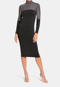 Robe midi noire scintillante à manches longues et col montant. Présente une silhouette ajustée et un tissu texturé lumineux, associée à des talons transparents.