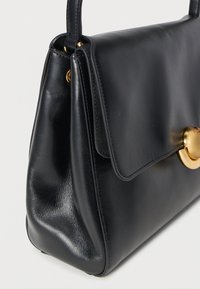 Sort læderhåndtaske med klaffelukning, der har guldfarvet cirkulært beslag. Glat overflade og struktureret form med diskrete syningsdetaljer.
