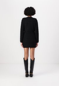 Rochie mini texturată, de culoare neagră, cu mâneci lungi și siluetă ajustată, asortată cu cizme din piele neagră până la genunchi, decorate cu accente din lanțuri aurii.